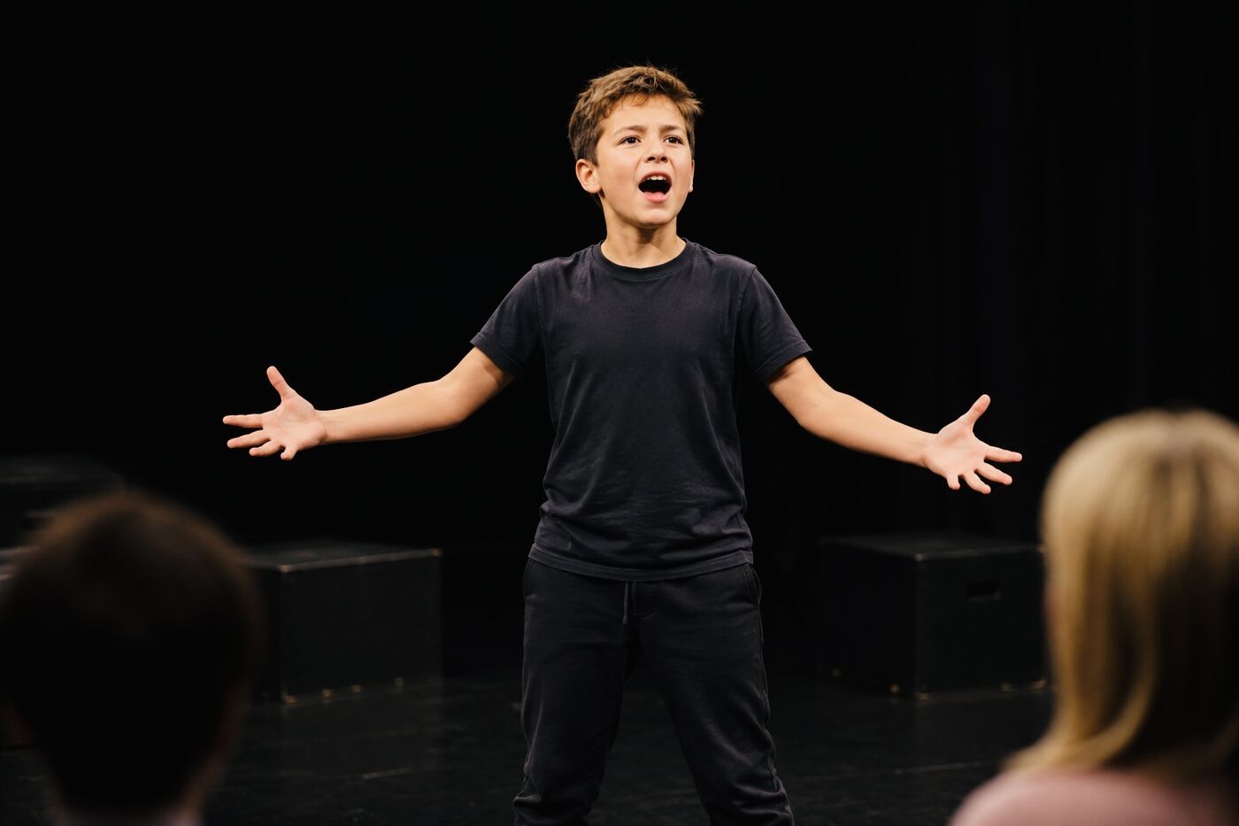 A young student performing a monologue on stage, arms outstretched