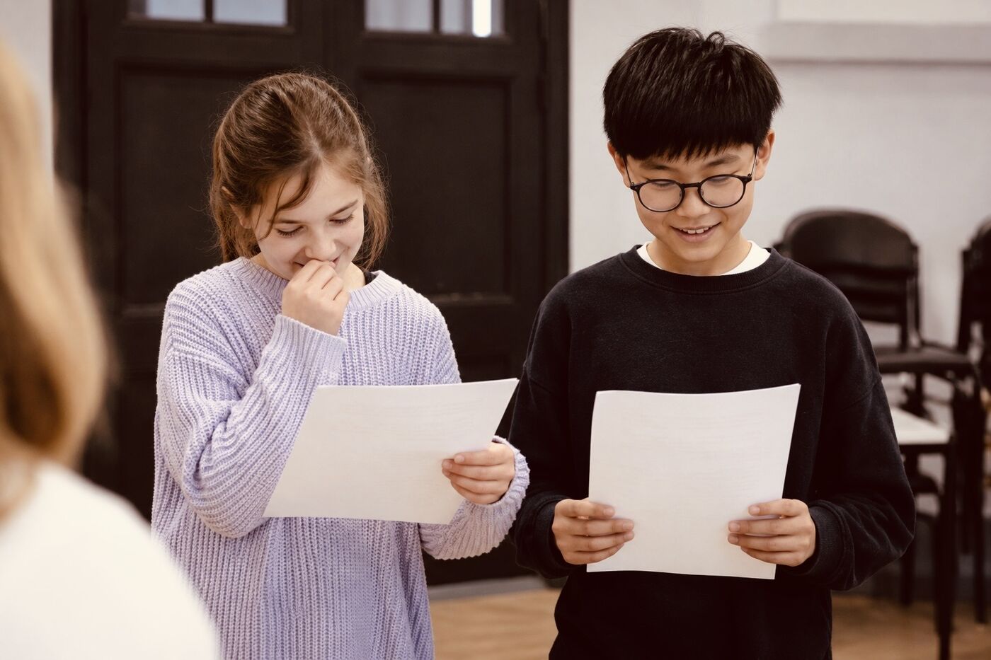 Two younger students reading from scripts in a lesson